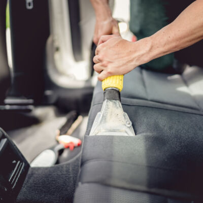 Car detailing and car care concept - Professional using steam vacuum for draining stains